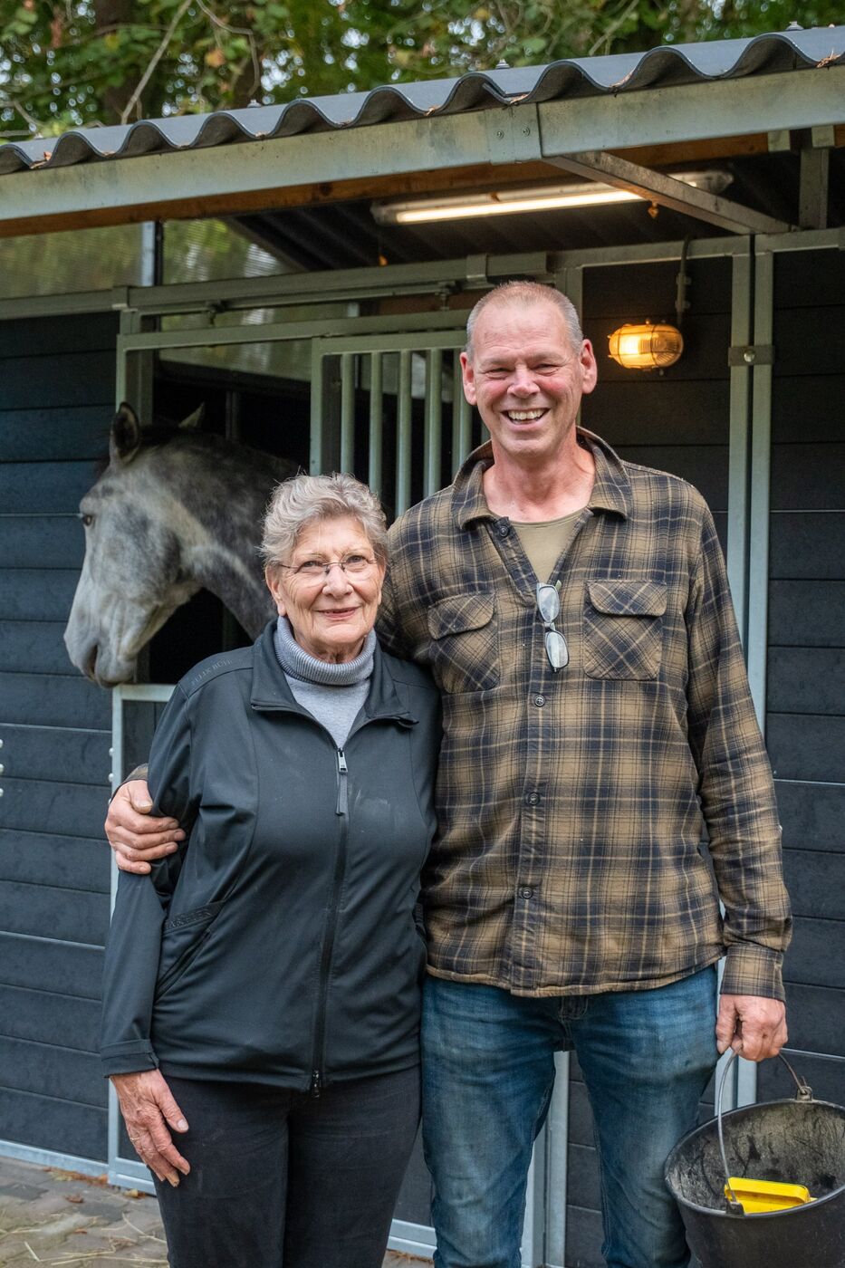 André en Loes voor de paardenstal, met een schimmel die nieuwsgierig meekijkt